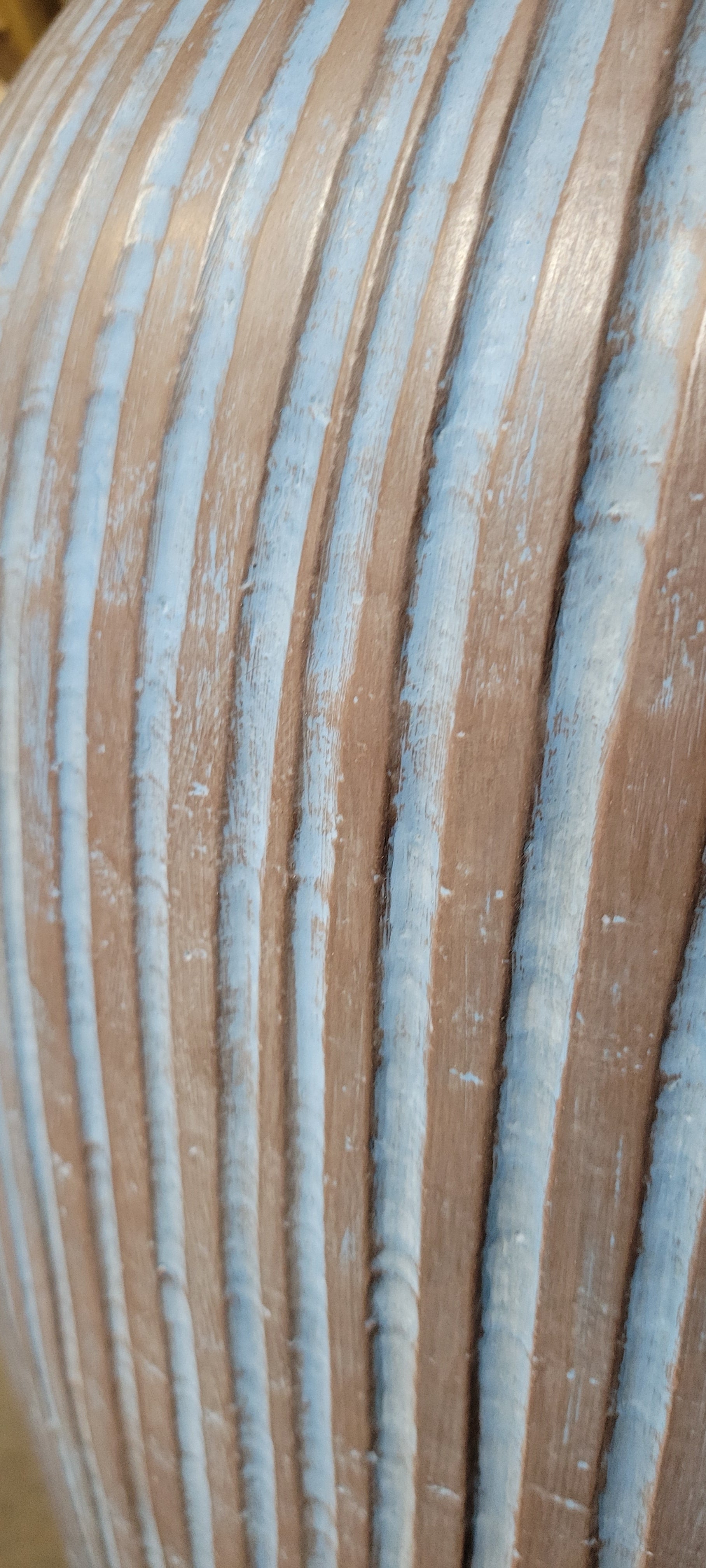 Close-up studio photo of the side section of a ribbed terracotta vase in soft blue and earthy brown tones with gentle lighting highlighting its textured surface.