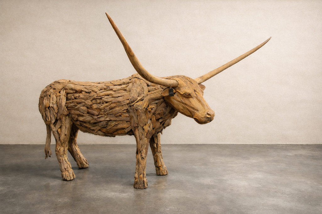 Life-size longhorn sculpture made from reclaimed teak wood, shown in a studio on a concrete floor. Natural layered wood texture, wide curved horns.